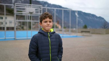 One thoughtful young boy walking outside at city park during winter season with hands in pocket. Pensive male preteen kid strolling in contemplation