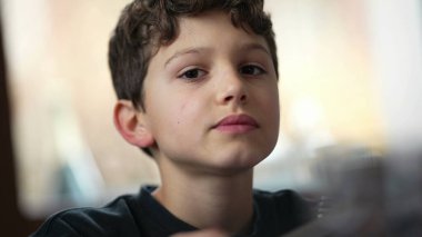 Yemek masasında yemek çiğneyen küçük bir çocuk. Ergen çocukların yemek yediği gizli bir yüz ifadesi. Düşünceli ifade