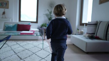 Evin içinde koşan küçük bir çocuğun arkasında. Modern bir apartman dairesinde enerji dolu bir çocuk. Küçük çocuk koşucu