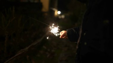 Child hands holding fire sparkler outside celebrating holidays