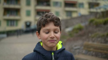 Parkta ileri doğru yürüyen dalgın bir genç çocuk. Üzerinde kışlık giysiler olan düşünceli bir çocuk şehir parkında yürüyor.