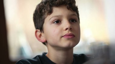 Yemek masasında yemek çiğneyen küçük bir çocuk. Ergen çocukların yemek yediği gizli bir yüz ifadesi. Düşünceli ifade