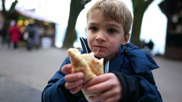 stock image One little boy eating food outside in street during winter season. Child eats warm pancake outdoors in city during winter season