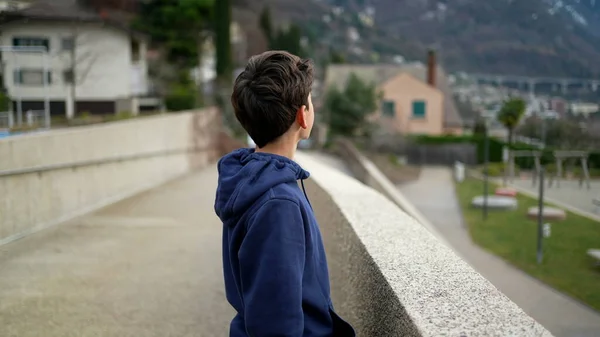 Teen kid stands at park outside staring at horizon in meditation. Tracking shot of young boy in contemplation