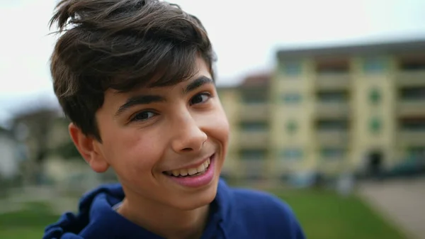 Portrait of a happy teenager young boy standing outdoors at park looking at camera in tracking shot. Closeup face of a male kid