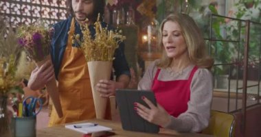 Female business boss delegating orders to male employee inside flower shop. Florist entrepreneur sending online orders delivery