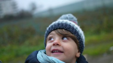 One happy little boy wearing winter clothes smiling at parent while strolling outdoors in city sidewalk