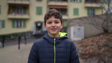 Dışarıda kameraya doğru ilerleyen, kışlık ceketli bir çocuğun portresi. Yakışıklı çocuk dışarı çıkıyor.