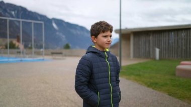 One thoughtful young boy walking outside at city park during winter season with hands in pocket. Pensive male preteen kid strolling in contemplation