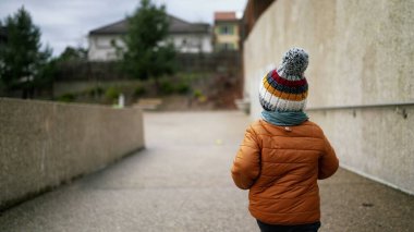 Küçük bir çocuk kış mevsiminde şehir parkında koşuyor.