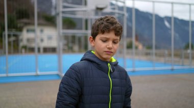 One thoughtful young boy walking outside at city park during winter season with hands in pocket. Pensive male preteen kid strolling in contemplation