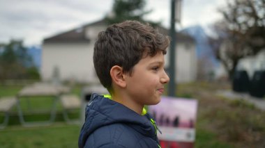 Portrait of a young boy walking outside in city park smiling. Handsome preteen kid strolling outdoors. Tracking shot of a happy male child wearing winter jacket