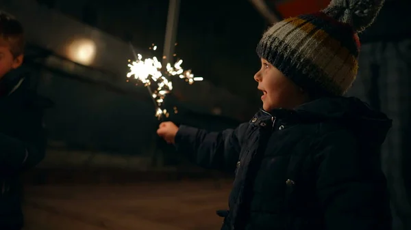 Happy child holding fire sparkler at night celebrating Christmas holidays in december