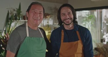 Employees portrait faces with happy expression. A Japanese mature small business entrepreneur with male young staff wearing aprons. Job occupation concept