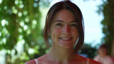 30 'lu yaşlarda mutlu bir kadın, yakından kameraya bakıyor. Açık havada duran çekici bir kadın.