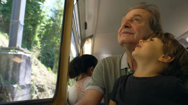 stock image Grandfather traveling by train with small grandson seated on lap by window. Grandparent bonding with baby grandchild doing tourism together on railroad transportation