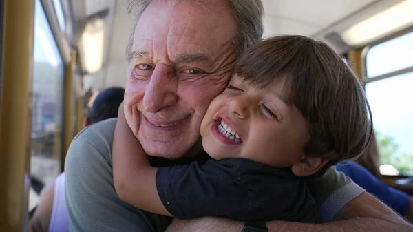 Grandson hugging grandfather while traveling by train on vacation. Child embraces senior grandparent cheek to cheek on railroad. Generational love