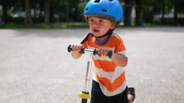 Genç çocuk dışarıda kaskla scooter kullanıyor. Aktif bir çocuk yaz güneşli bir günde üç tekerlekli oyuncak taşımacılığı yapıyor.