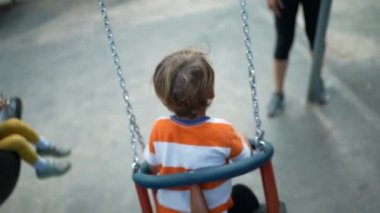 Çocuk salıncakta sallanıyor. Park Swing 'te çocuğu iten bir ebeveyn. Aile hafta sonu etkinliği