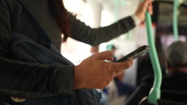 Yüz maskesi takan bir kadın otobüsün içindeki telefona bakıyor.