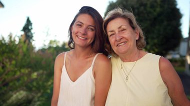 Yaz günü dışarıda kameraya poz veren olgun kadın ve genç gelinin portresi. Farklı nesillerden iki mutlu kadın.