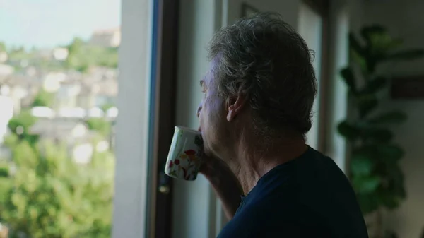 Emerytowany Starszy Pan Pijący Kawę Lub Herbatę Przez Okno Domu — Zdjęcie stockowe