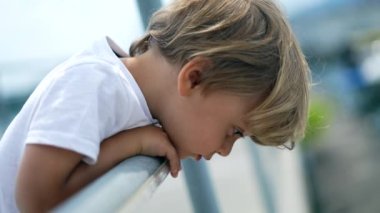 Köprünün dışındaki tırabzanlara yaslanmış düşünceli küçük bir çocuk. Düşünceli bir ifadeyle. Meditasyon yapan erkek sarışın çocuk hayatı düşünüyor.