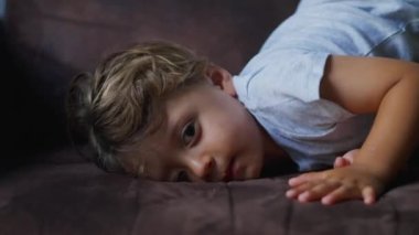 Küçük çocuk kanepede baş aşağı yatıyor. Evde sabahları pijama giymiş tatlı bir çocuğun kanepede yattığı hayat tarzı.