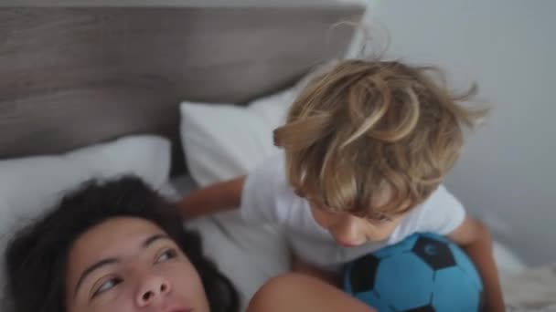 小男孩抱着妈妈在床上咬了一口 有趣的真实生活家庭生活关系在周末互动 幸福的概念 — 图库视频影像