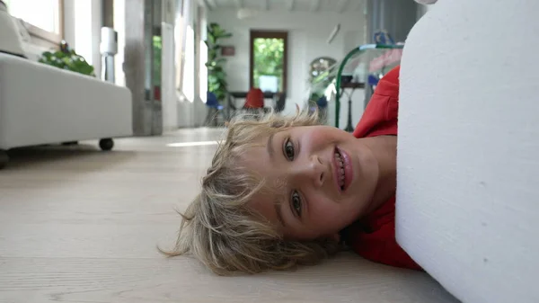 一个快乐的小男孩躲在现代家居客厅的沙发后面 躺在地板上 — 图库照片