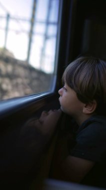 Trenle seyahat eden küçük bir çocuk. Pencereden dışarı bakan bir çocuk. Dikey Video