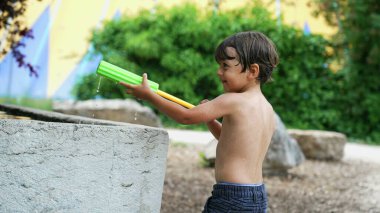 Yaz günü köpüklü oyuncak su savaşı sırasında çocuklara su püskürtmek. Islak çocuk tatilin tadını çıkarıyor.