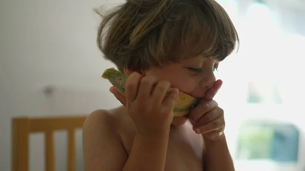Child biting melon fruit dessert. One young boy eating healthy tasty snack close up face
