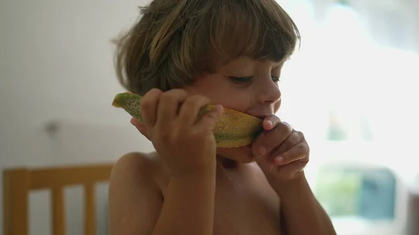 Child biting melon fruit dessert. One young boy eating healthy tasty snack close up face