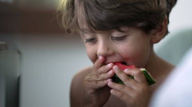 Gizli çocuk kırmızı karpuz meyvesinden bir ısırık alıyor. Sağlıklı meyve yiyen küçük bir çocuk.