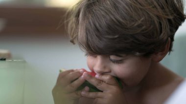 Candid child taking a bite of red watermelon fruit. One small boy eating healthy fruit
