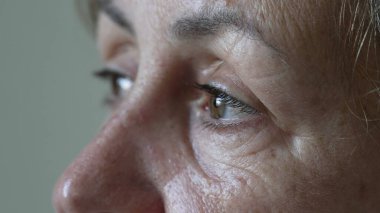 A thoughtful senior woman with contemplative expression macro eyes close up. One mature older female person in 70s looking at horizon daydreaming clipart