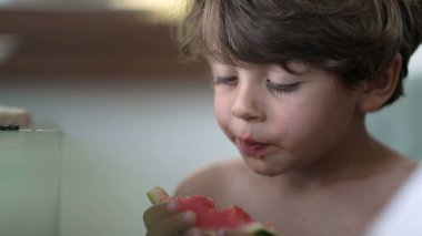 Candid child taking a bite of red watermelon fruit. One small boy eating healthy fruit