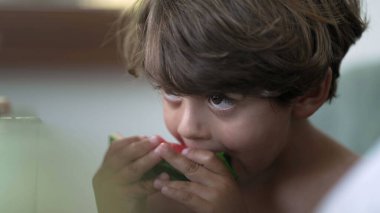 Candid child taking a bite of red watermelon fruit. One small boy eating healthy fruit