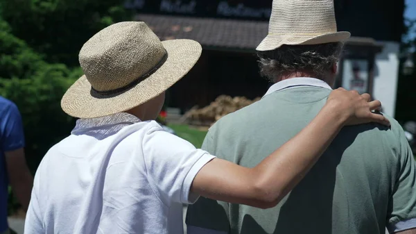 阳光灿烂的日子里 儿子身穿巴拿马帽 抱着父亲 手挽手走在外面 — 图库照片