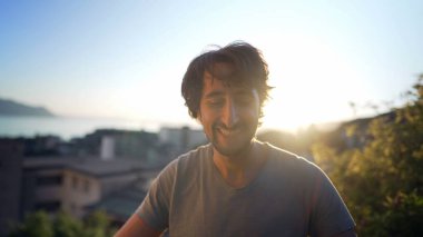 Portrait of a happy man in 30s standing outdoors in sunset time overlooking landscape in background. Close up face male person