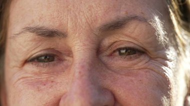 Happy senior woman macro eyes close up looking at camera. Wrinkled female person in 70s aged expression