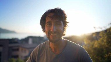 Portrait of a happy man in 30s standing outdoors in sunset time overlooking landscape in background. Close up face male person