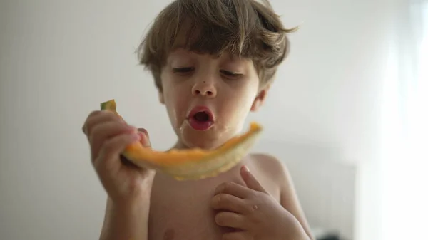 一个小男孩在屋里吃着黄色的瓜果 小孩儿在吃健康零食时的肖像脸特写 — 图库照片