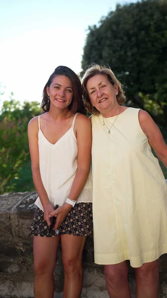 Portrait of mature woman and young daughter in law posing for camera standing outdoors during summer day. Two happy women of different generations