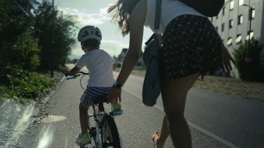 Anne yardımı ve desteği ile dışarıda bisiklet sürmeyi öğrenen bir çocuk. Küçük çocuk dışarıda bisiklet sürüyor.