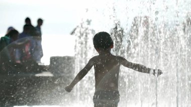 Sıcak yaz gününde, küçük bir çocuğun şehirdeki su parkı jetlerinde oynarken görüntüsü bulanık.