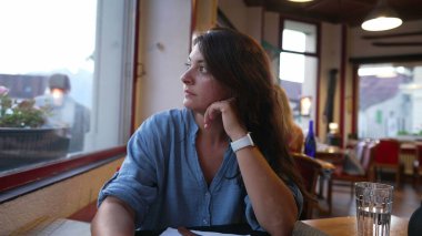 Düşüncelere dalmış 30 'lu yaşlarda bir kadın restoranda oturmuş pencereden dışarı bakıyor. Düşünceli kadın, yemeğin gelmesini bekliyor.