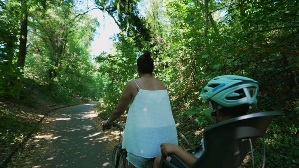 マウンテンバイクの後部座席に座っている子供と一緒に自転車に乗っている母親は — ストック写真