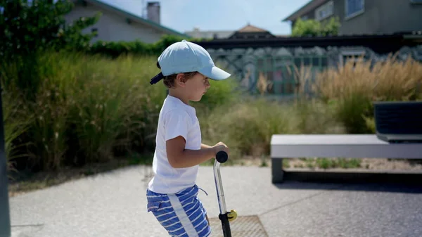 stock image Little boy riding 3 wheeled scooter outside. Happy child rides toy